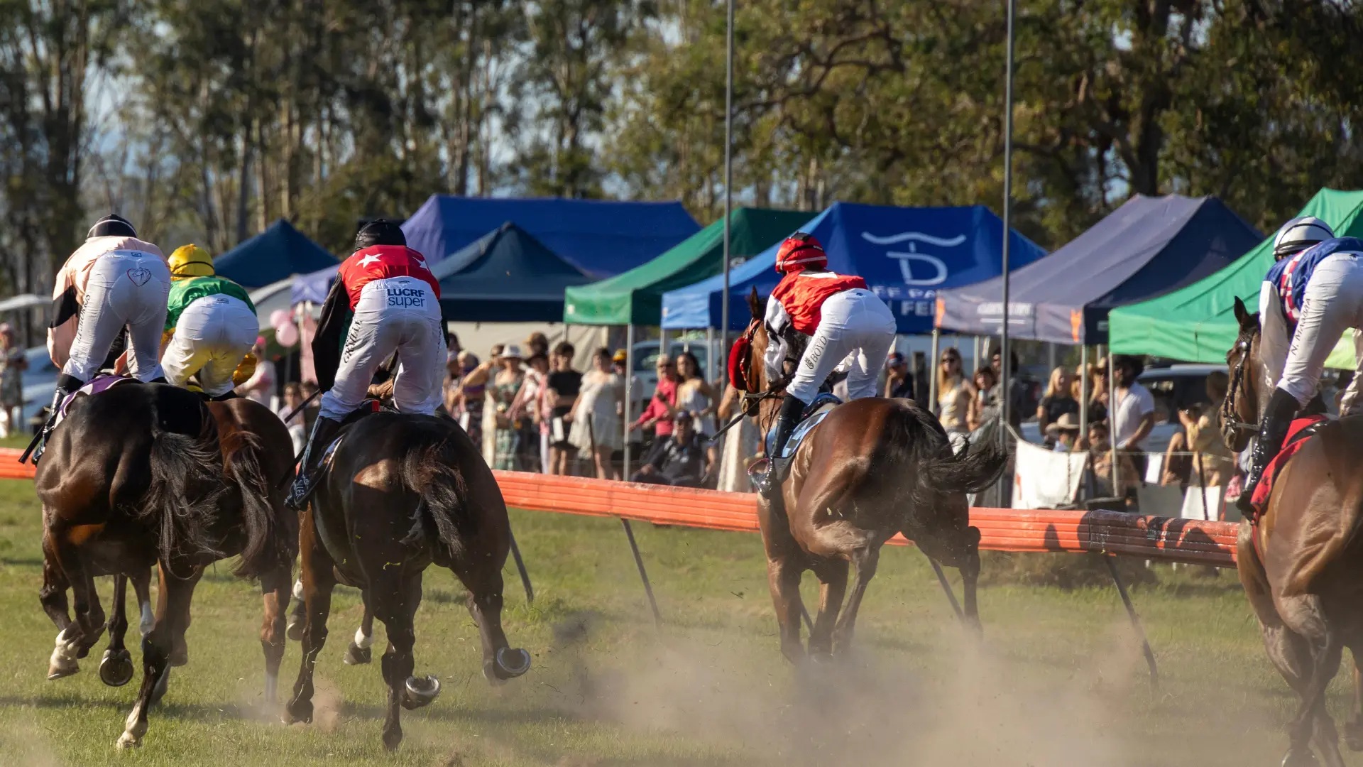 Horses and jockeys rounding the turn past the crowd at Tabulam Race Day
